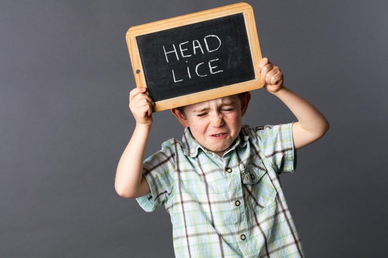Slika deteta u košulji koje drži crnu tablu na kojoj piše na engleskom "Head lice"